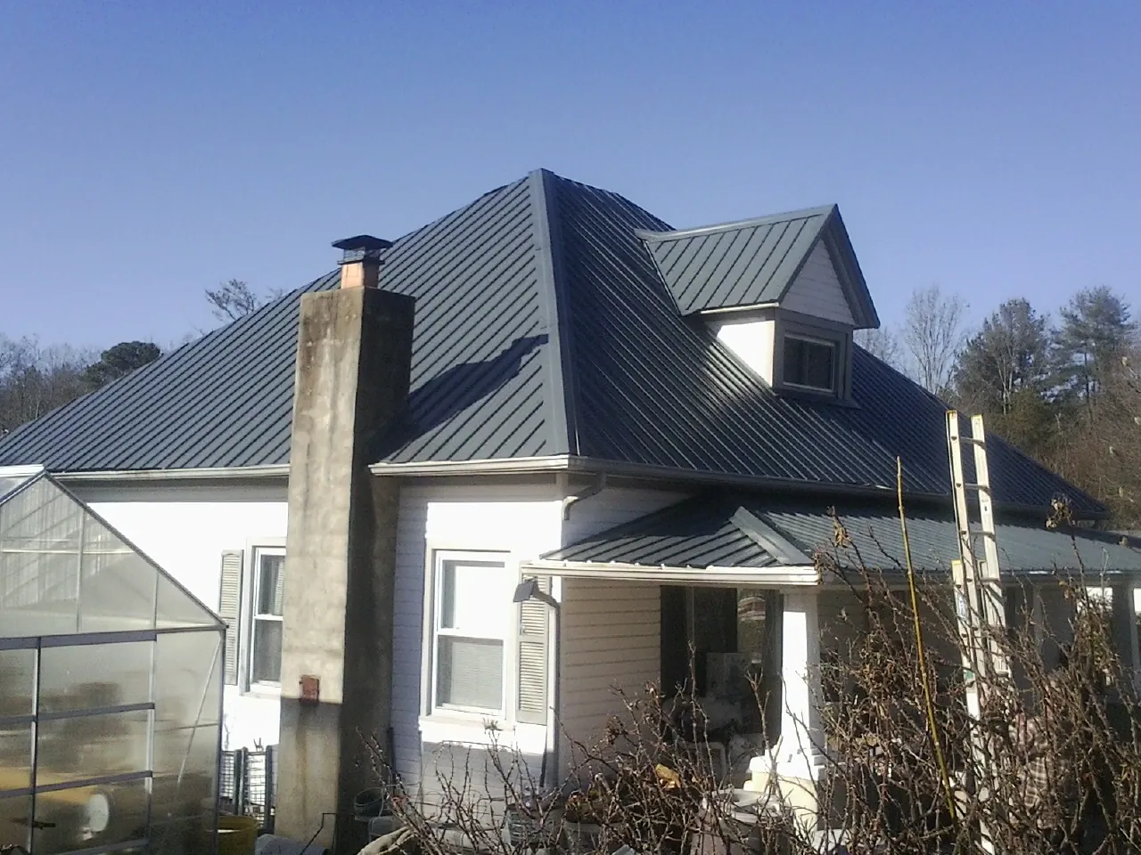 Dark blue standing seam metal roof on a white farmhouse with dormer — Slate & Tile Roof Repair by Roofing Brothers in Rosine