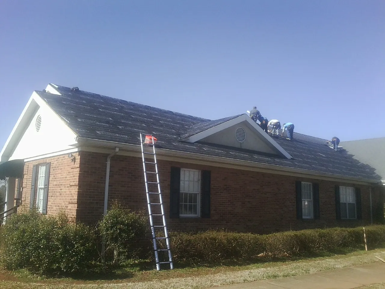 Crew tearing shingles off a brick ranch roof with a ladder set — Emergency Roof Repair work by our crew in Rosine