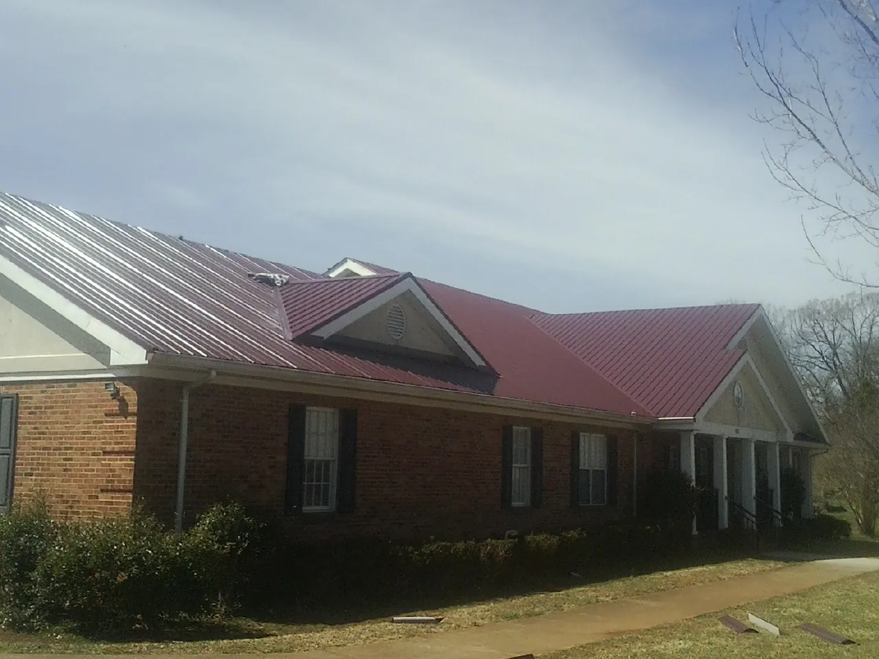 Red metal roof with gabled entries on a long brick building, from a Hail Damage Roof Repair job in Rosine