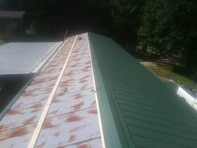 Old rusted panels beside newly installed green metal roofing — Wind Damage Roof Repair by Roofing Brothers in Rosine