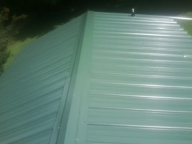 New green metal panels meeting at the ridge of a roof — Flat Roof Repair work by our crew in Rosine