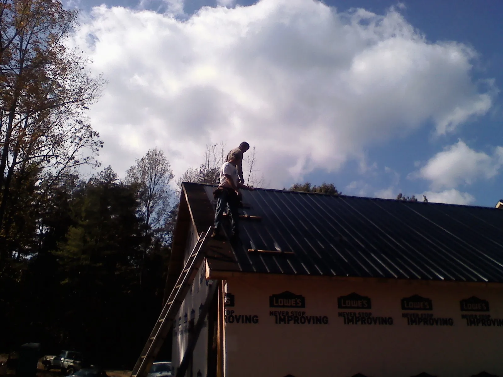 Roofer fastening dark metal panels high against a cloudy sky, from a Roof Inspection job in Rosine