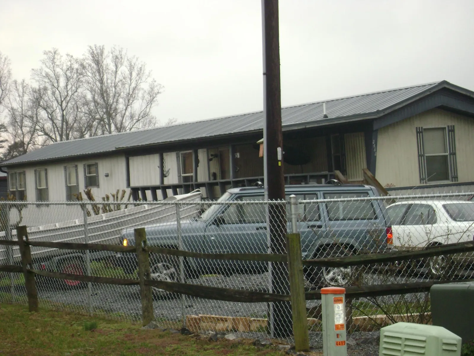 Dark metal roof on a long single story building behind a chain link fence in Rosine