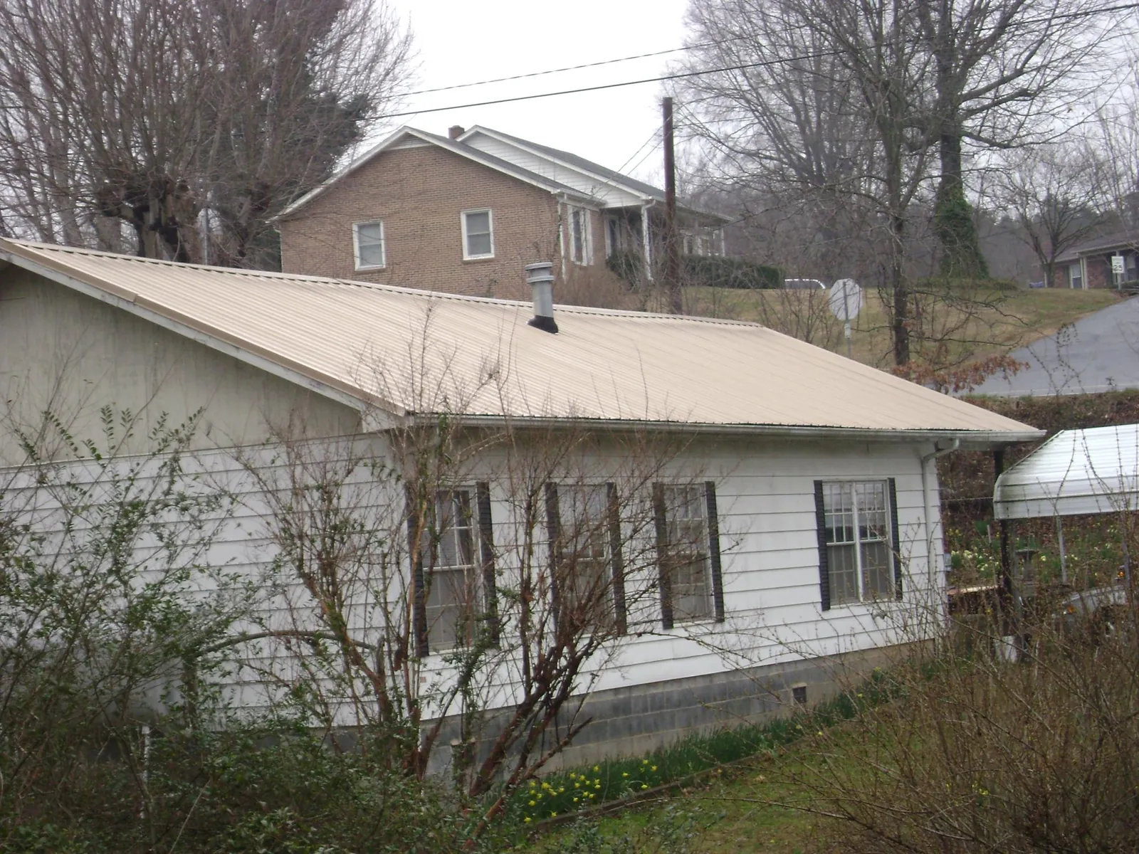 Tan metal roof on a white sided house set into a hillside — Commercial Roofing by Roofing Brothers in Rosine