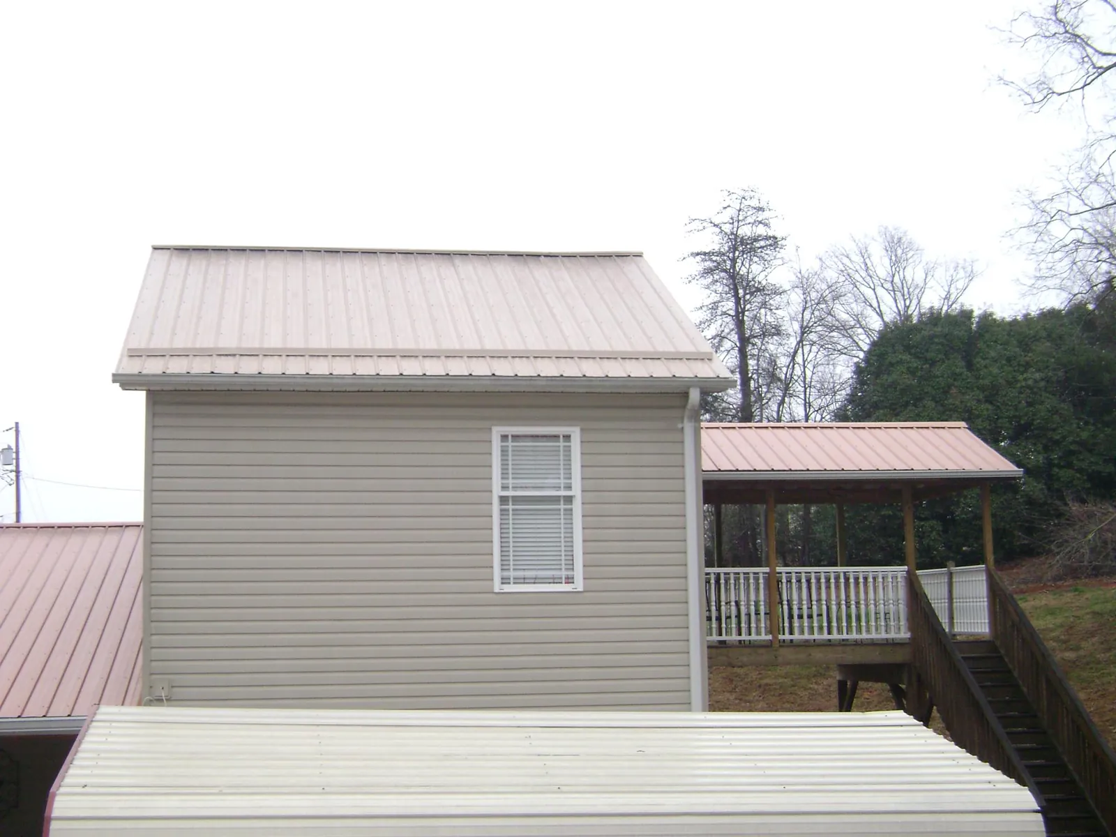 Tan metal roofs on a two story addition and attached porch, from a Roof Replacement job in Rosine